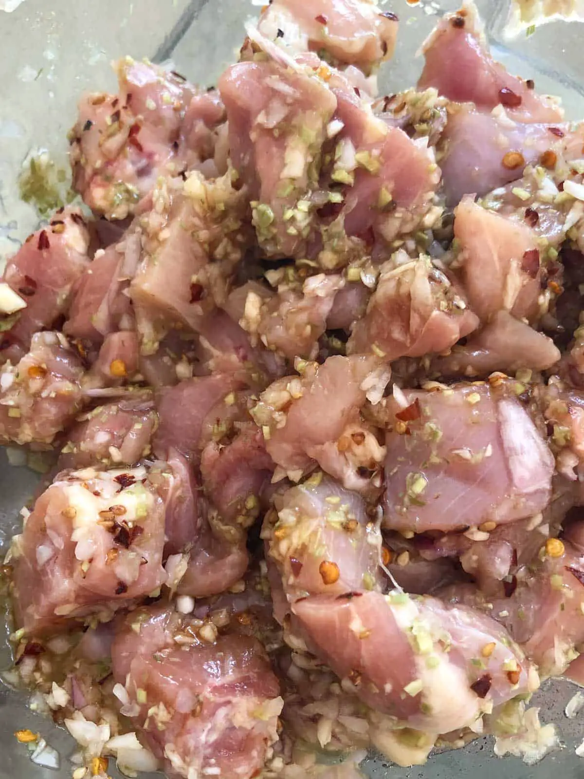 Uncooked pieces of chicken marinating with lemongrass, chili flakes, shallots and minced garlic.