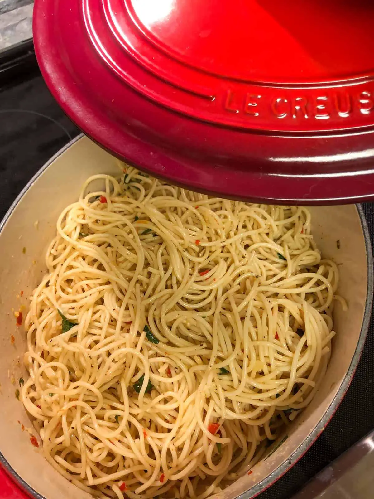 A red Le Creuset dutch oven containing spaghetti with the red lid being held above it.