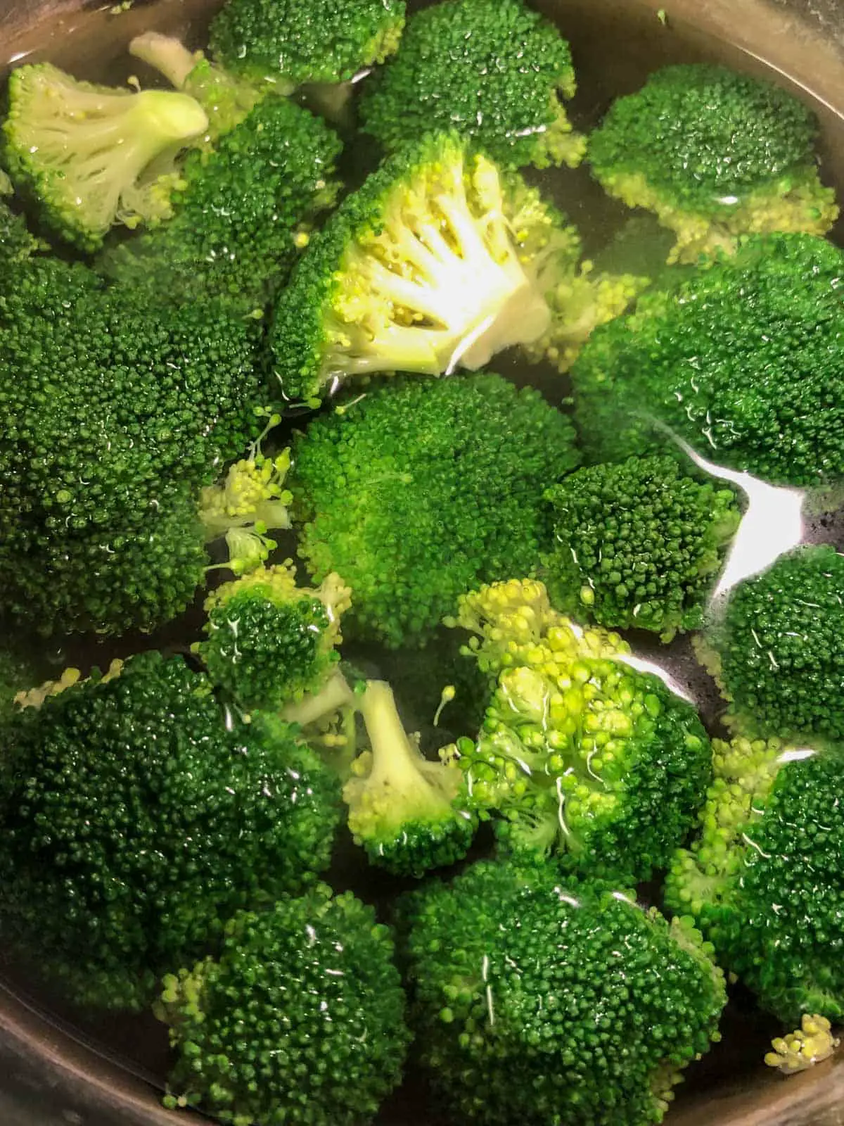 Broccoli florets in water in a large pot.