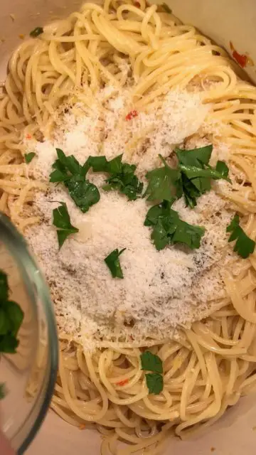 Spaghetti in a dutch oven with grated Parmesan cheese and chopped Italian parsley on top of the spaghetti.