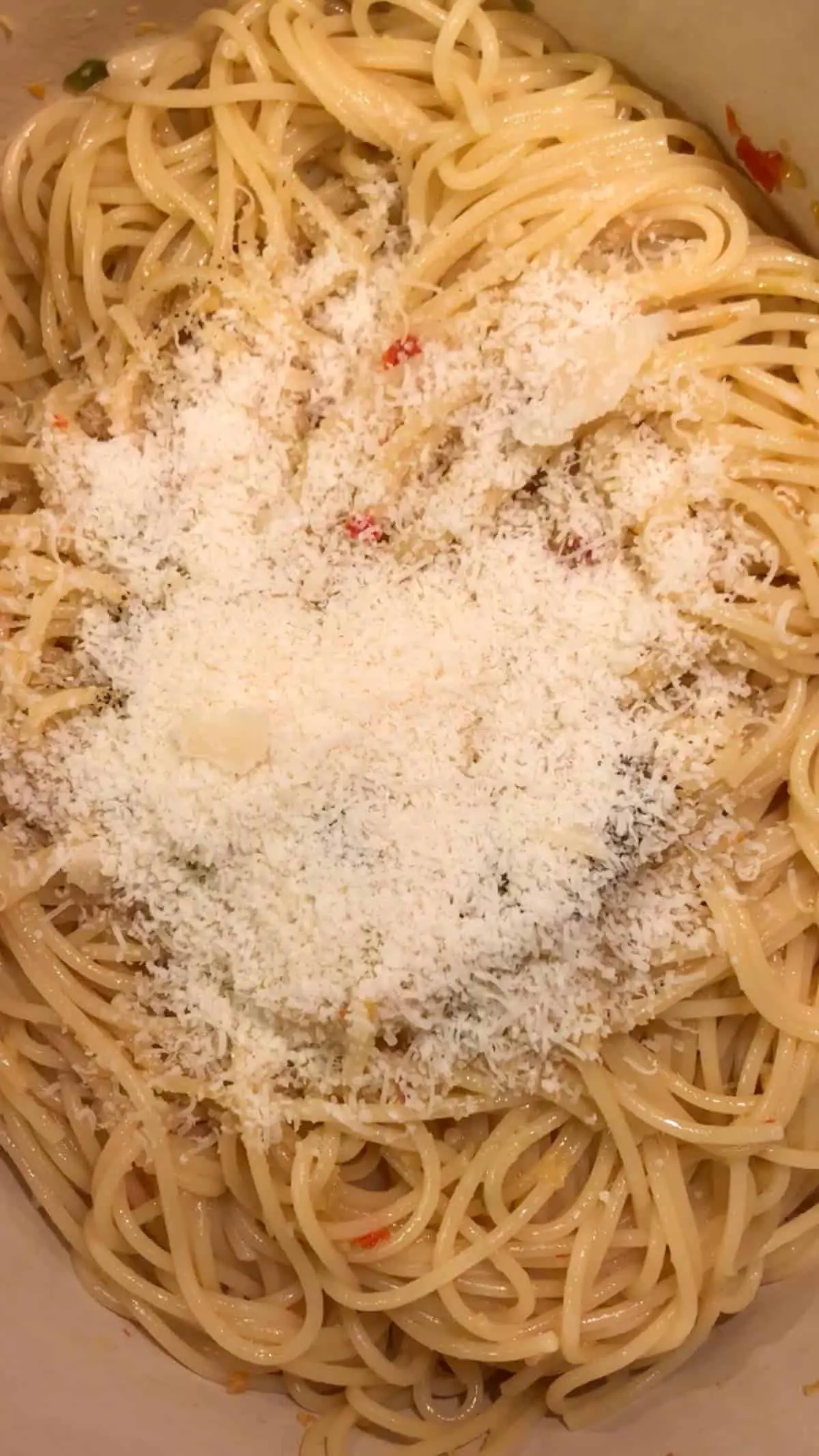 Spaghetti in a dutch oven with grated Parmesan cheese on top of the spaghetti.