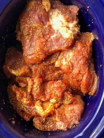 Seasoned pork cuts of meat in a blue crockpot.