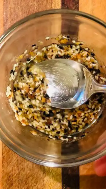Everything Bagel seasoning with melted butter and a spoon stirring these to combine them in a glass bowl.