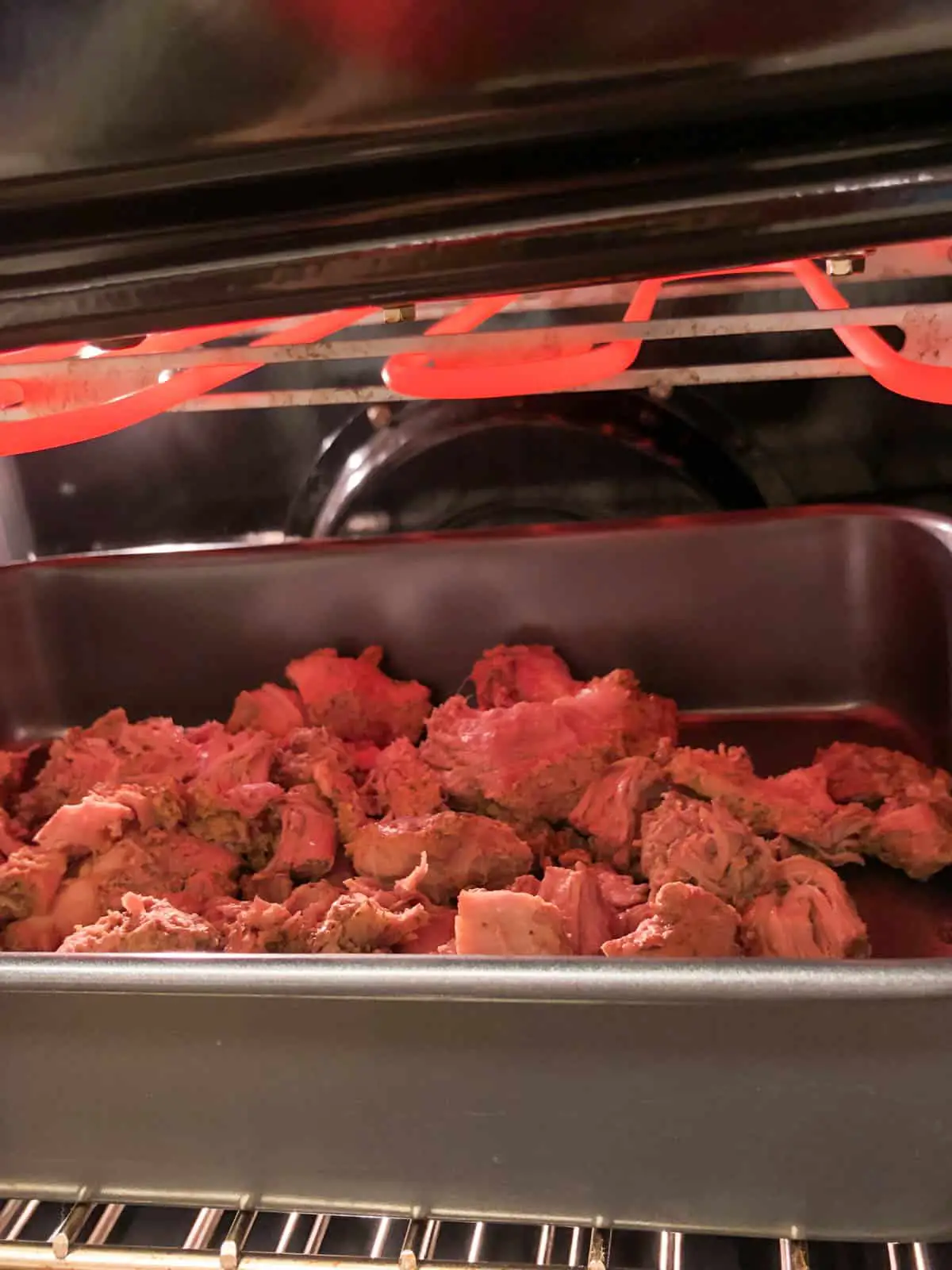 Pieces of pork in a roasting tray under a broiler.