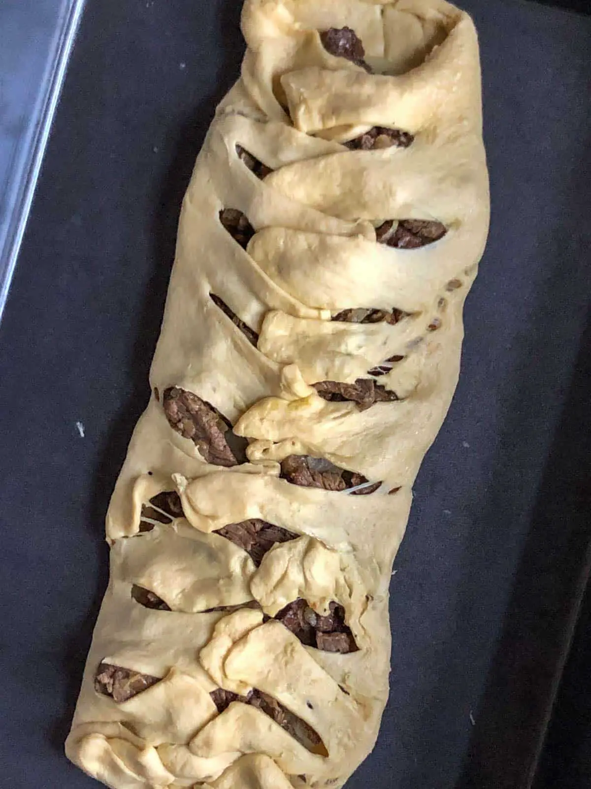 Sliced rib eye steak wrapped with crescent roll dough that has been cut into 1 inch intervals and placed on top of the sliced meat to resemble mummy wrappings.
