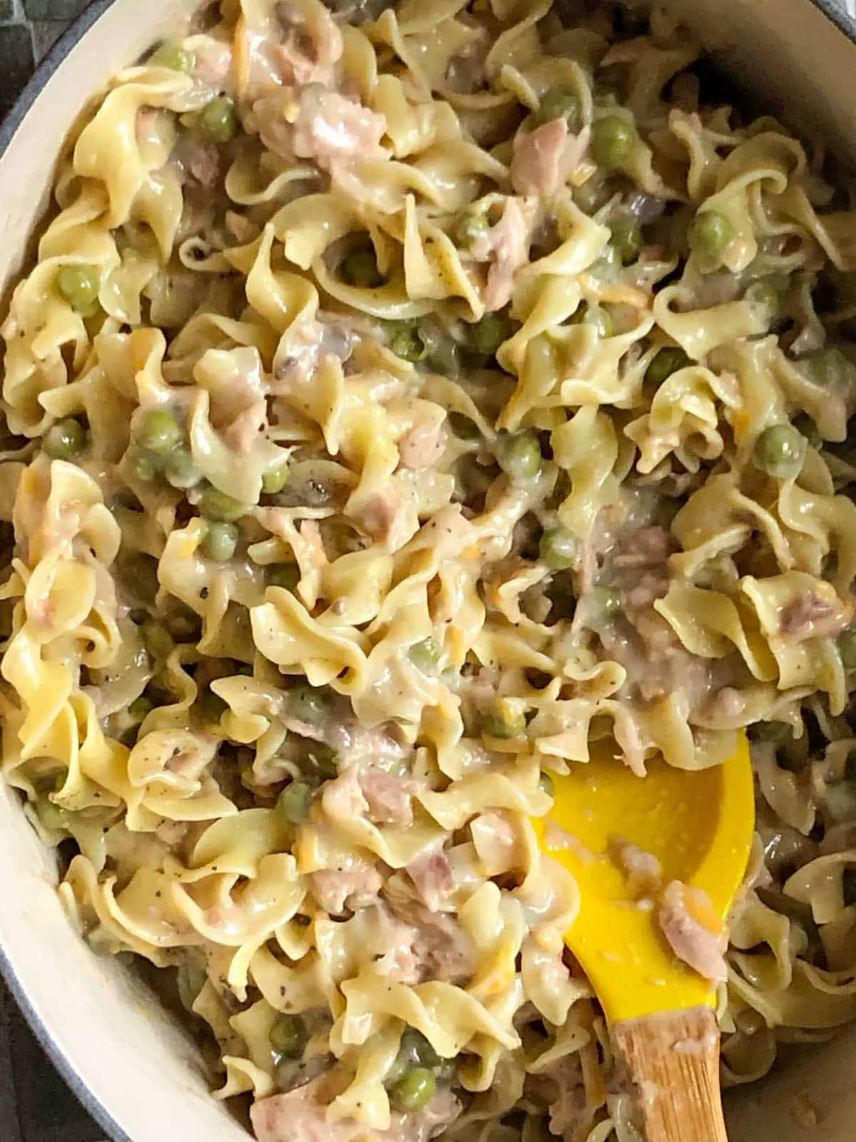 Noodles cooked with tuna and peas in a creamy sauce and a yellow spoon cradling some of the tuna noodle casserole.