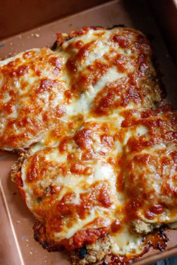Veal parmigiana which has been cooked with a topping of cheeses which have turned golden brown and melted in a roasting pan.