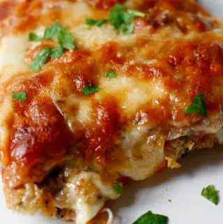 Veal parmigiana topped with melted cheese and garnished with Italian parsley on a white plate.