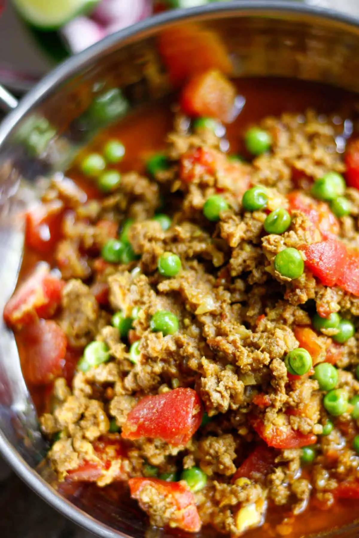 Lamb mince, peas, onion, and diced tomatoes in a rich sauce in a silver balti bowl.