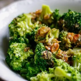 Broccoli florets in a white bowl with slivers of toasted garlic and a lemony sauce drizzled on top of the garlic.