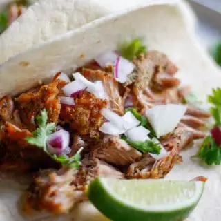 Shredded pork on flour tortillas garnished with onions, lime and cilantro.