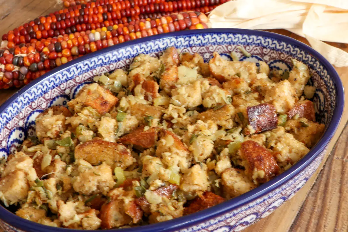 Sage and onion stuffing in a blue Polish pottery dish with colorful corn cobs in the background.