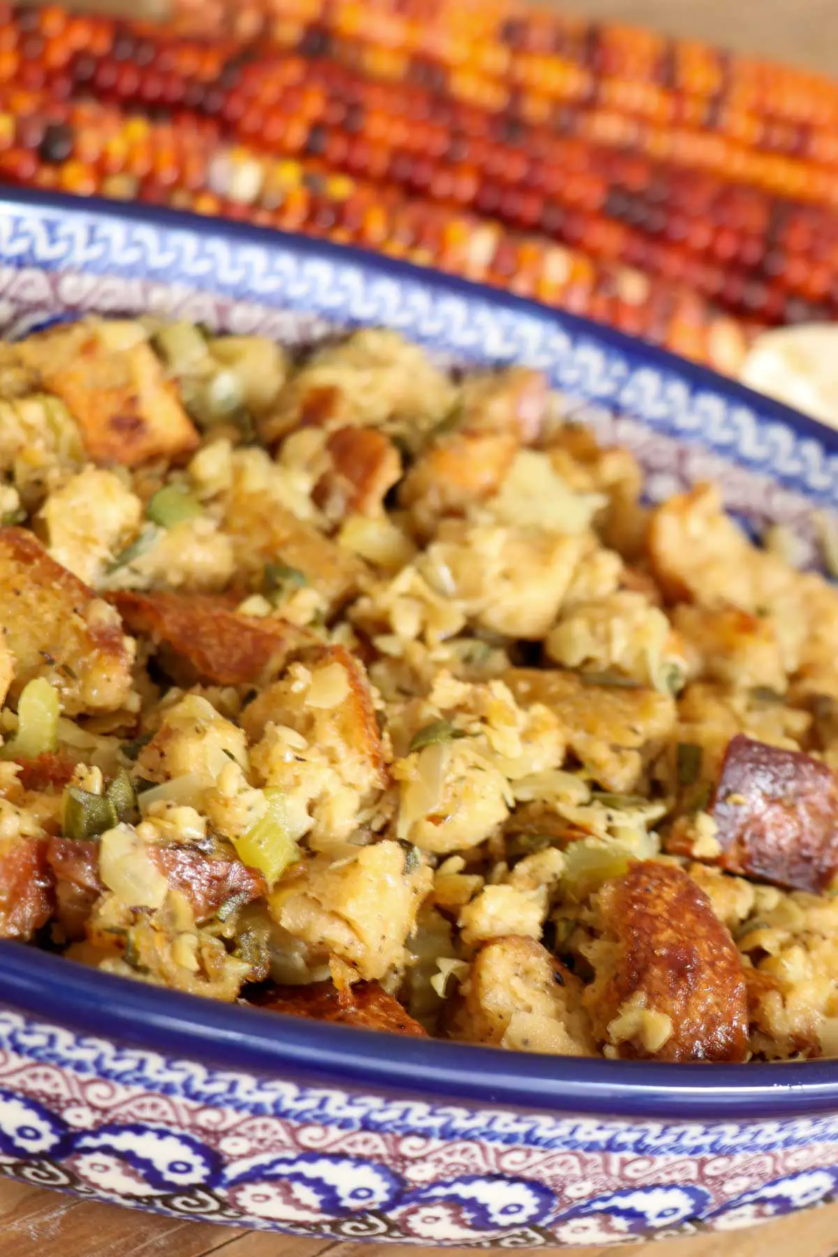 Sage and onion stuffing in a blue Polish pottery dish with colorful corn cobs in the background.