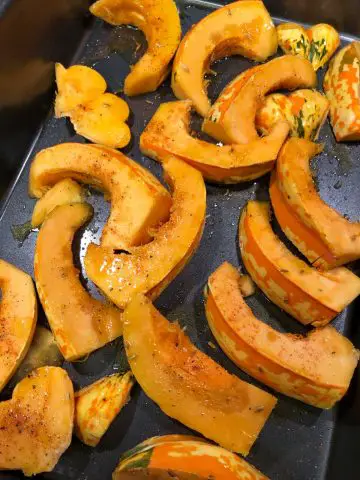 Wedges of carnival squash tossed with spices and olive oil in a roasting pan.