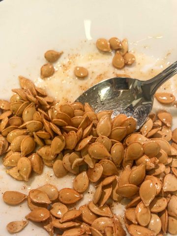 Roasted Carnival Squash Seeds with butter and seasoning added to them in a white dish with a silver spoon.