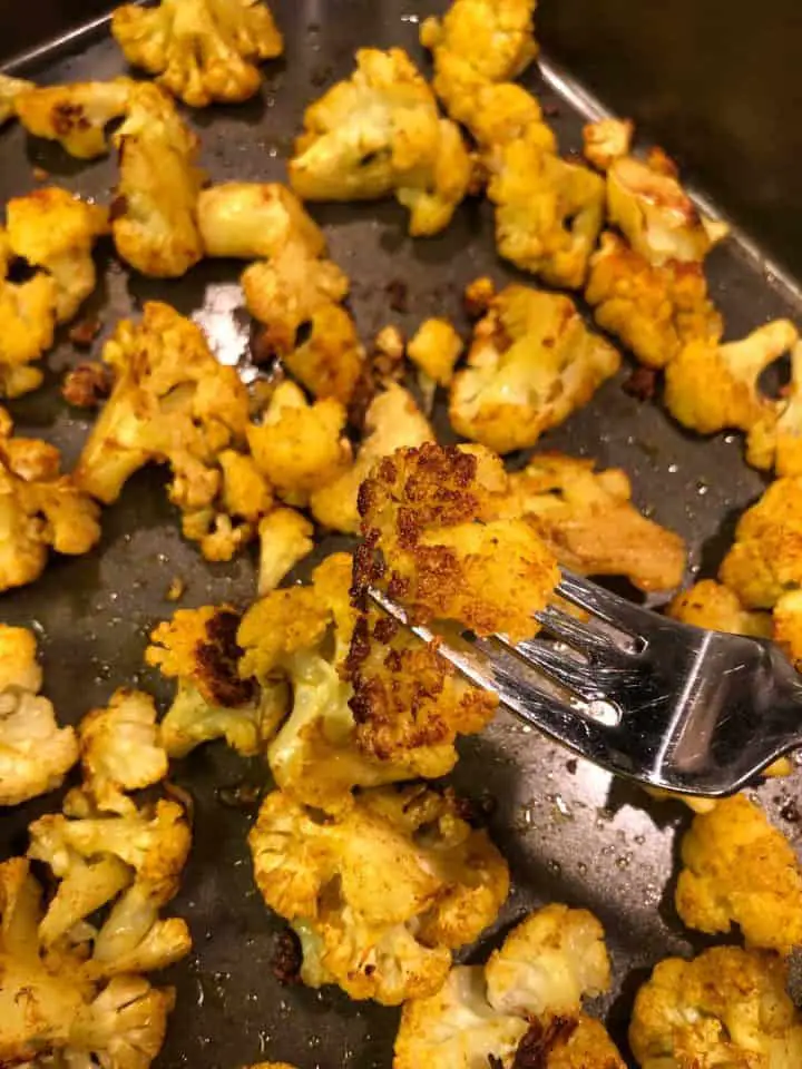 Tender cauliflower florets roasted with Indian spices with a fork piercing one of the florets to show how tender it is.