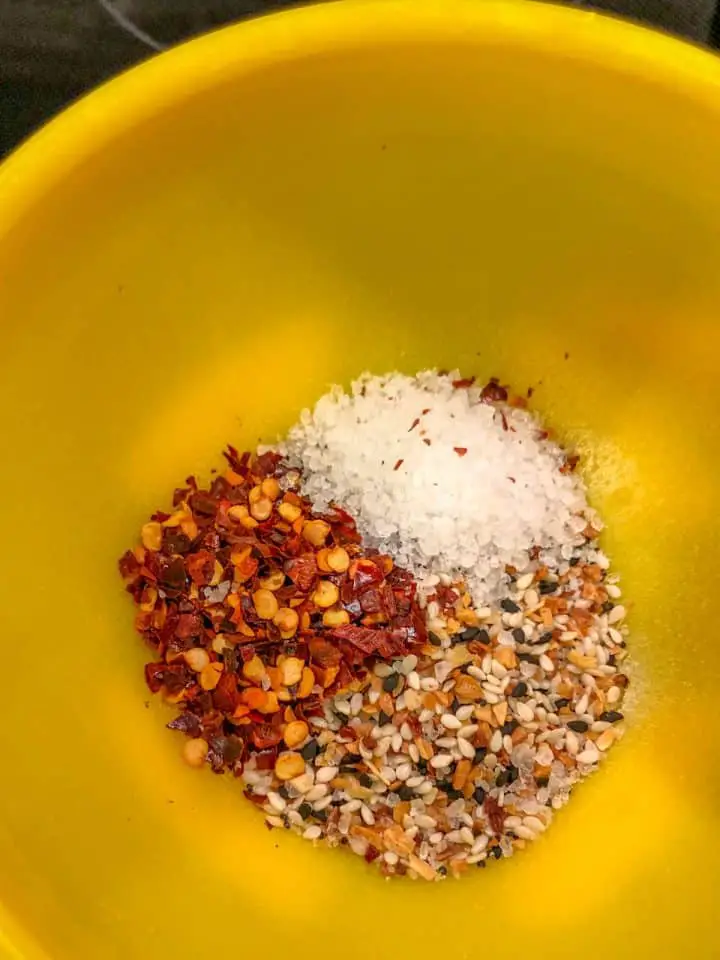Red chili flakes, coarse salt, and everything bagel seasoning in a yellow bowl.