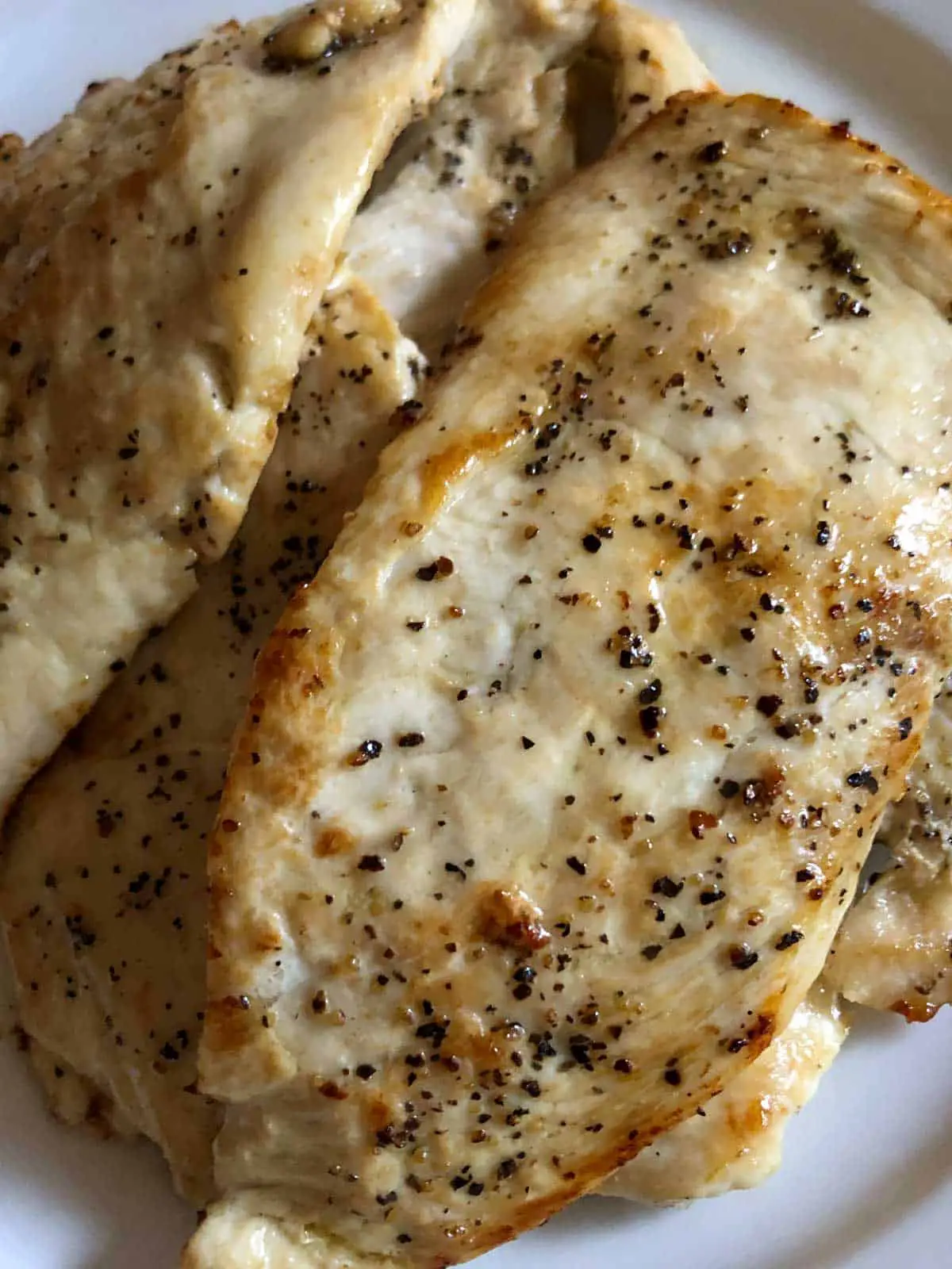 Chicken scallopini or thin slices of cooked chicken seasoned with salt and pepper on a white plate.