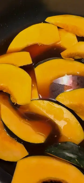 Wedges of acorn squash in a saucepan with soy braising liquid.