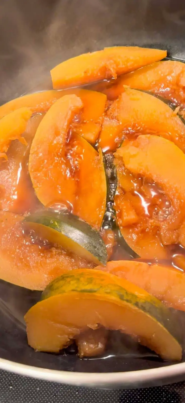 Wedges of acorn squash cooking in a saucepan with soy braising liquid and steam rising from the pan.