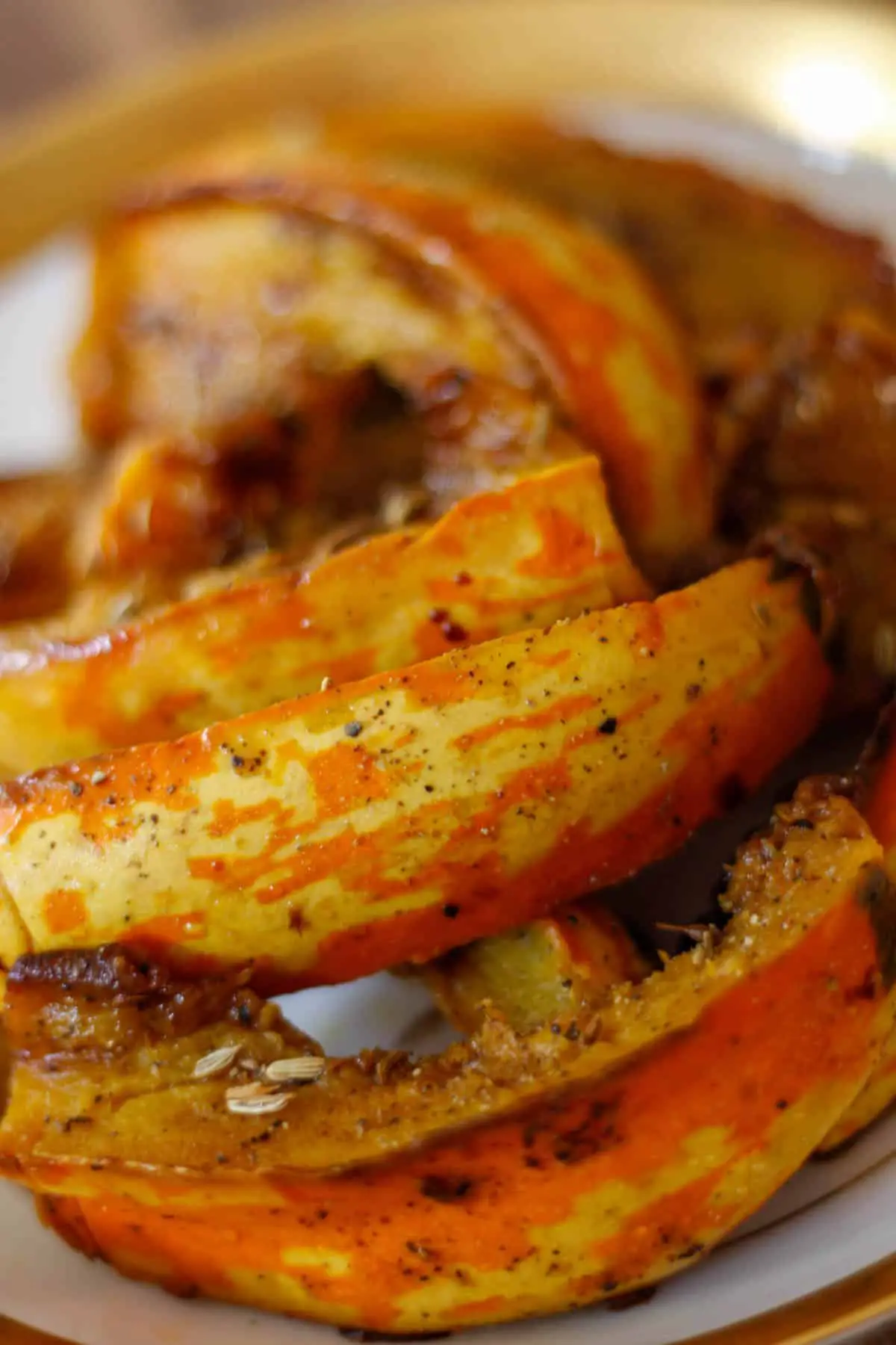 Wedges of carnival squash in a white gold rimmed bowl with fennel seeds and balsamic vinegar.