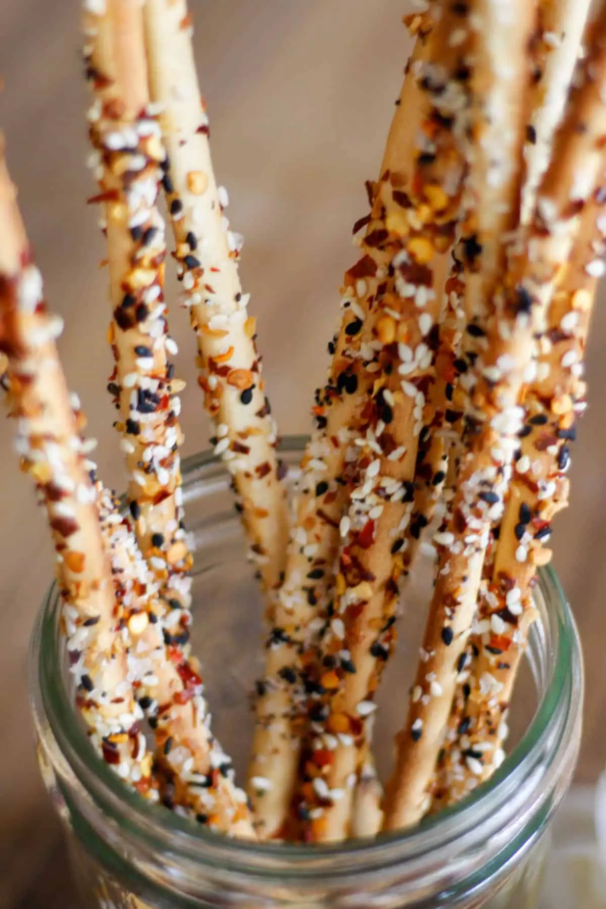 Thin breadsticks coated with everything bagel seasoning, salt and red chili flakes standing in a glass jar.