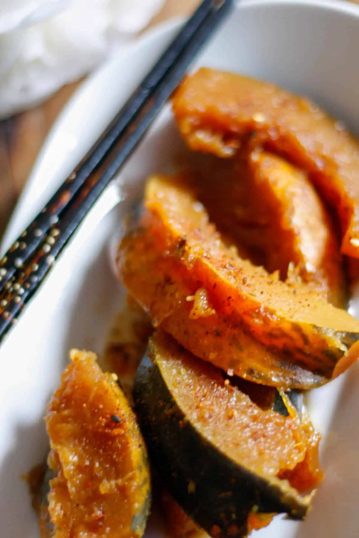 Wedges of cooked acorn squash with sprinkles of Japanese chili pepper on a white dish with chopsticks resting on the side.