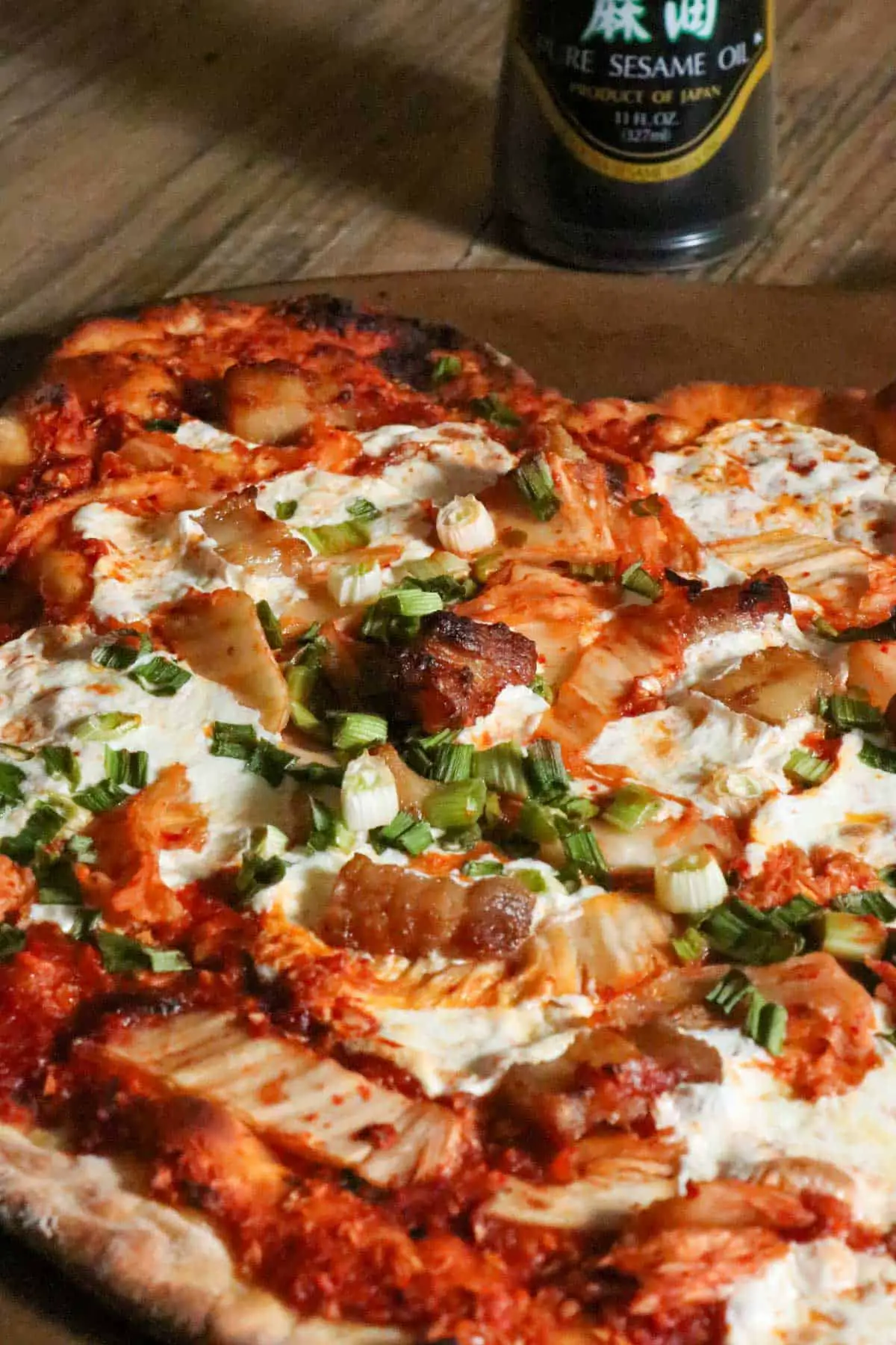 Pizza topped with mozzarella, kimchi, pork belly, tomato sauce, and green onions.