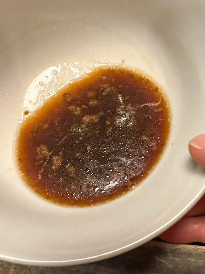 Coke red eye gravy in a white bowl held by a person whose fingers are visible.