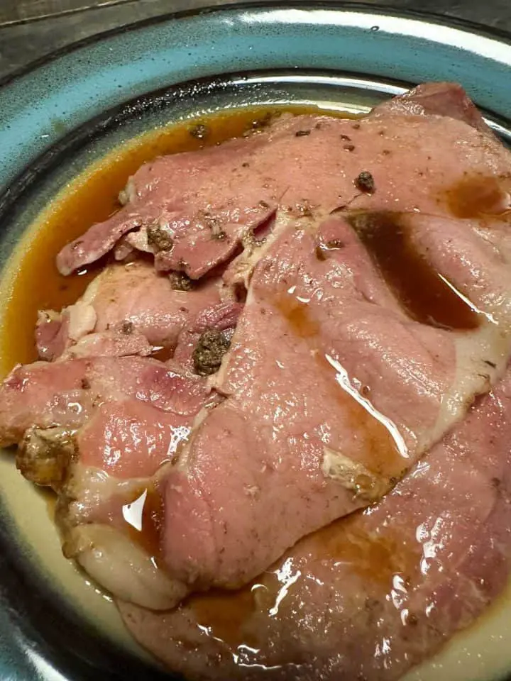A blue rimmed plate containing country ham slices with red eye gravy poured over them.