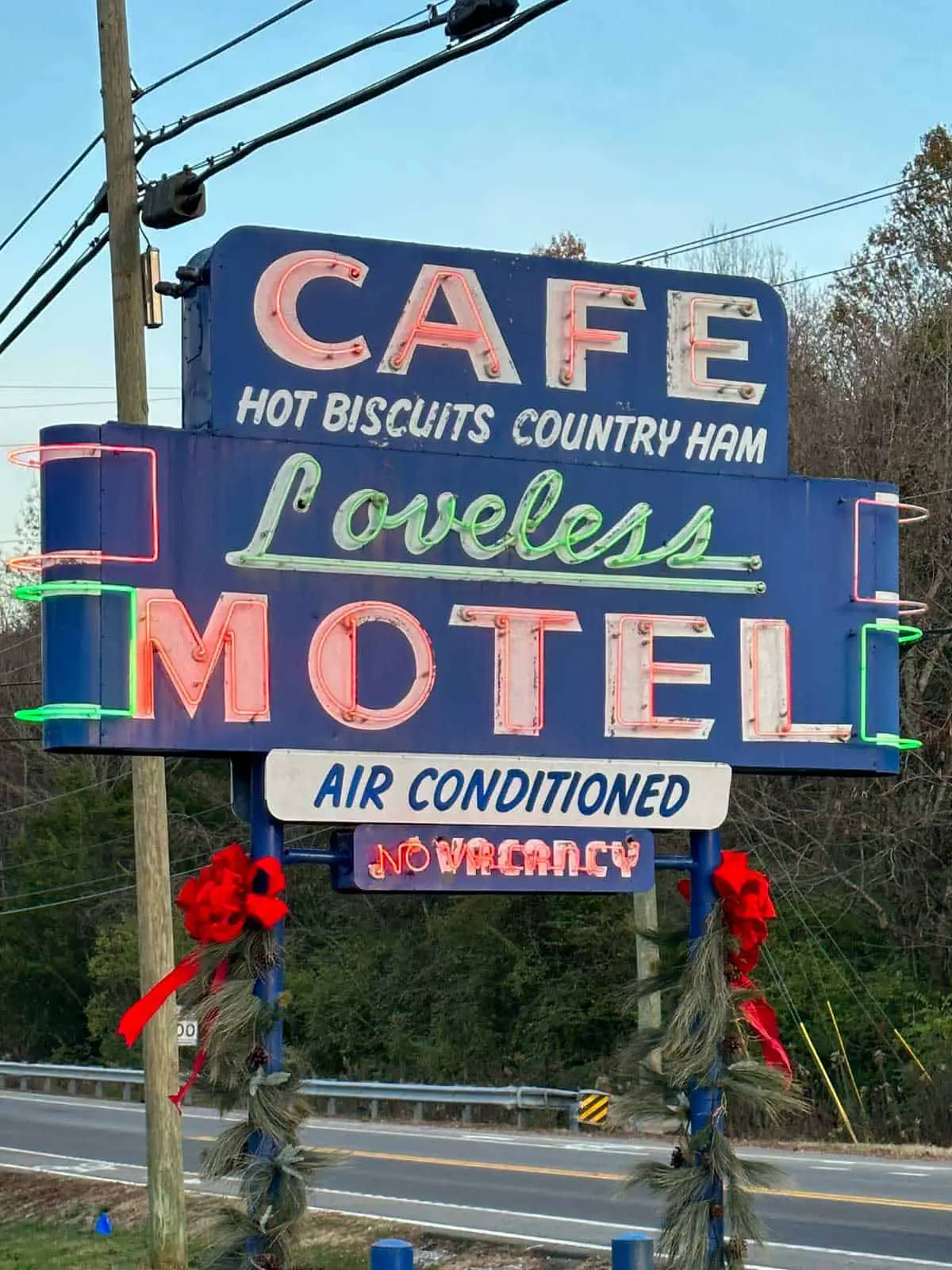 The Loveless Cafe sign which says cafe, Loveless Motel, air conditioned, no vacany, hot biscuits and country ham and the sign has red ribbons and wreaths wrapped around the poles.