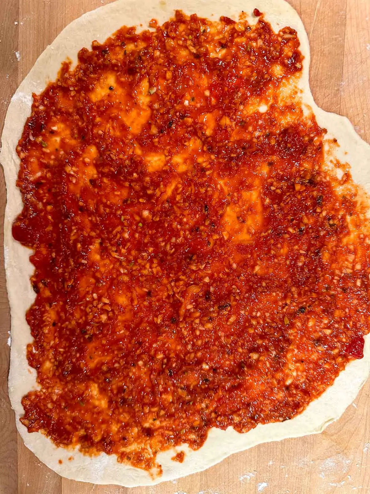 Uncooked pizza base topped with tomato sauce and garlic.