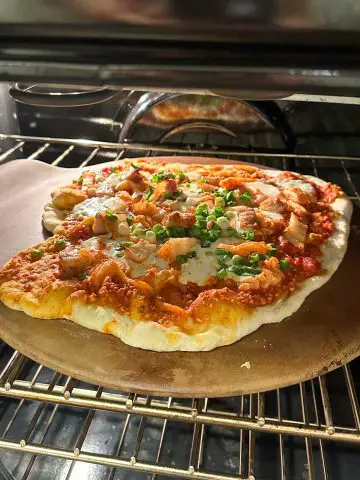 Kimchi pizza on top of a pizza stone baking in the oven.