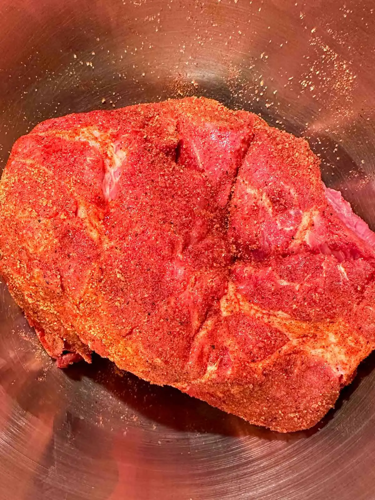 Pork butt seasoned with a dry rub in a metal bowl.