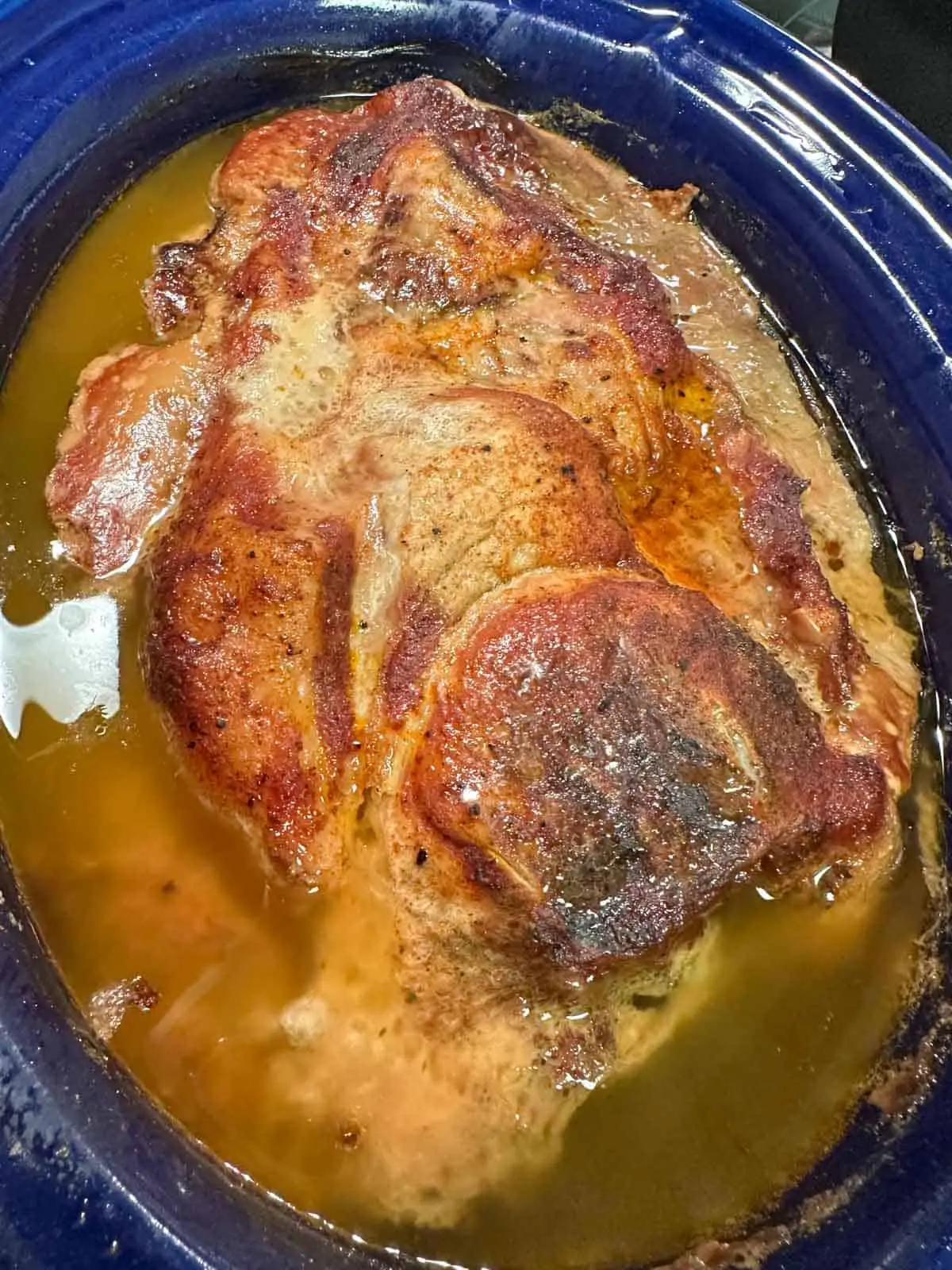 Pork which has been cooked in a blue slow cooker with its resulting broth from cooking.