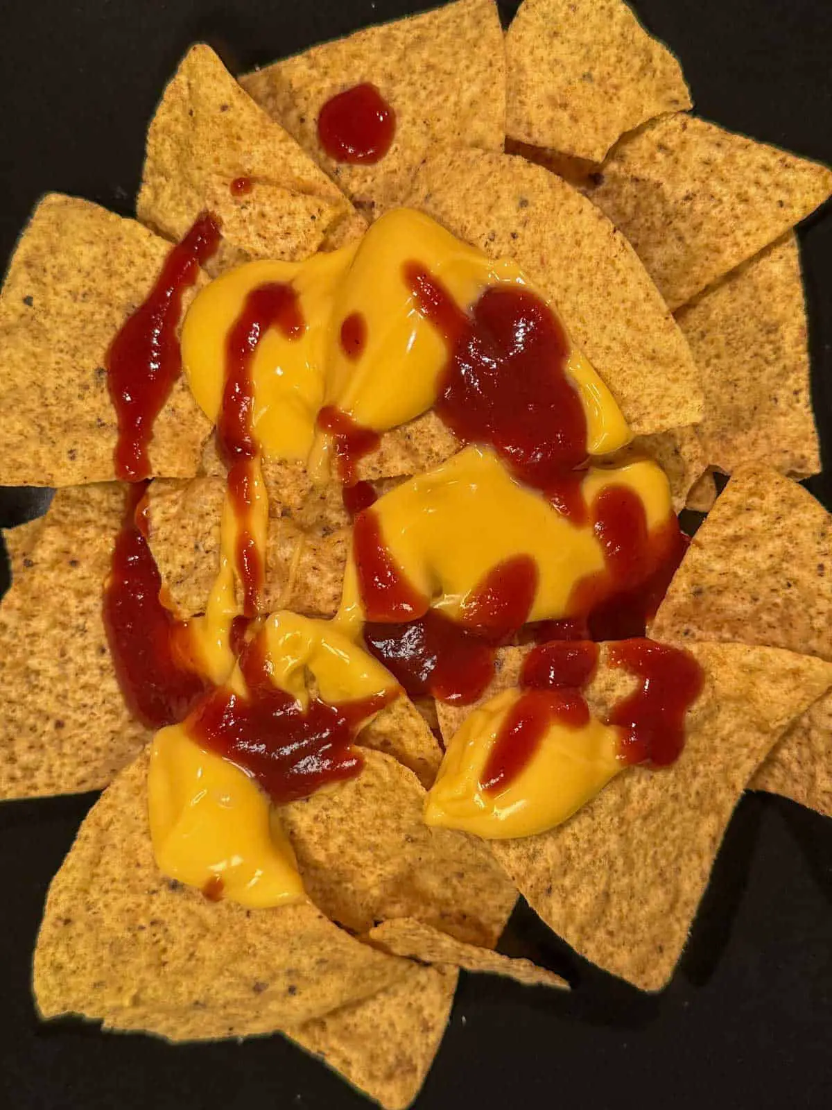 Tortilla chips topped with cheese sauce and barbecue sauce on a black plate.
