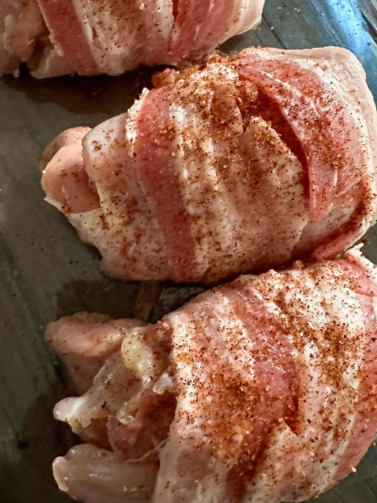 Uncooked chicken armadillo eggs which is chicken stuffed with sausage and wrapped with bacon with dry rub sprinkled on top.
