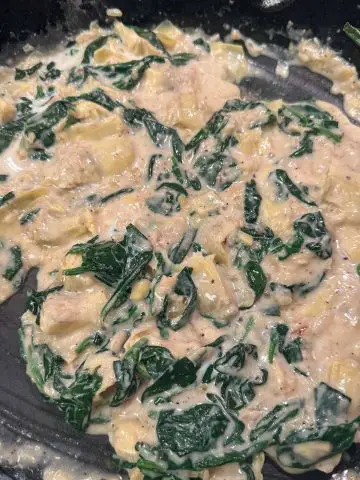 Wilted spinach and chopped artichokes in a creamy sauce cooked in a cast iron pan.