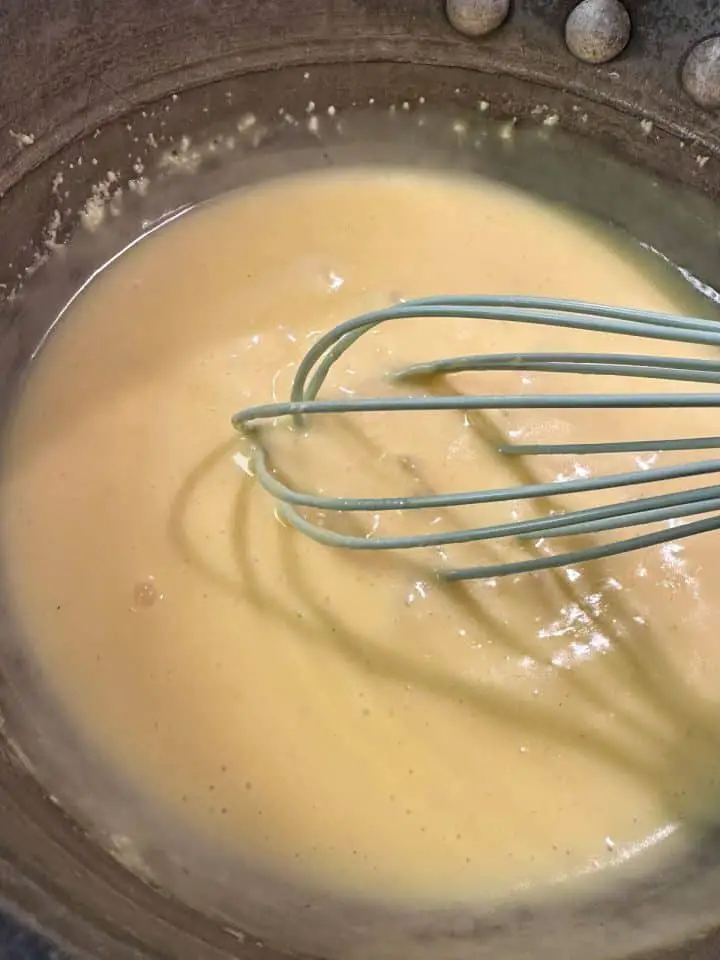 Prepared hollandaise sauce in a pan with a blue whisk.