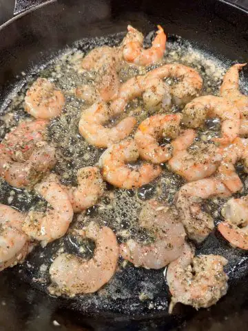 Shrimp cooking in a butter and olive oil sauce in a cast iron pan.