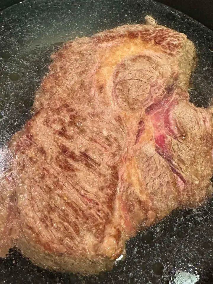 Beef chuck roast which has been browned covered with water in a pot.