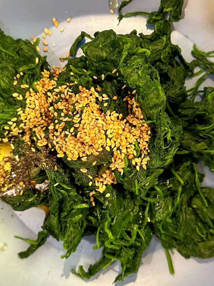 Wilted spinach combined with seasonings and sesame seeds in a blue bowl.