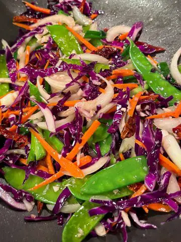 Snow peas, julienned carrots, sliced onions, sliced cabbage and dried Asian chilies in a wok.