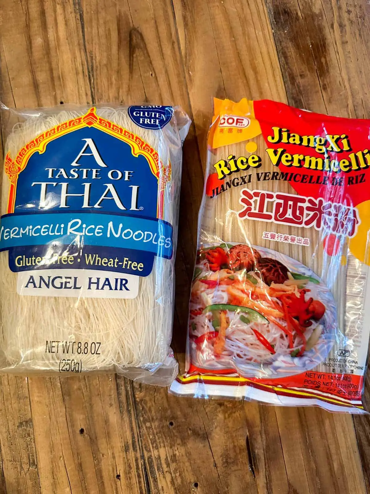 Package of A Taste of Thai Vermicelli Rice Noodles next to a package of Jiang Xi Rice Vermicelli Noodles on a wooden board background.