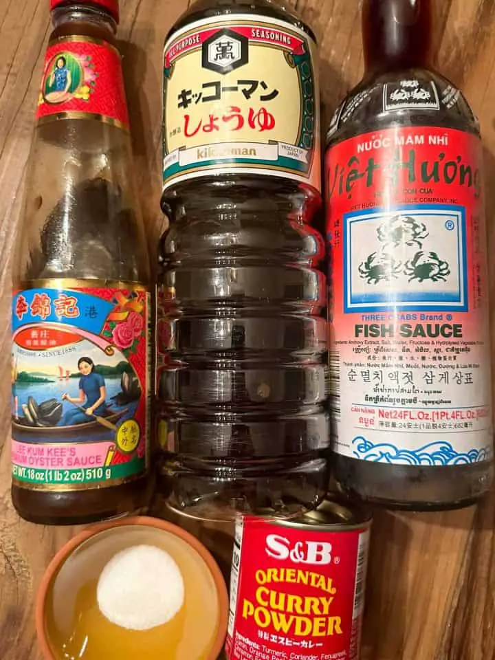 Bottles of oyster sauce, soy sauce, and fish sauce, a bowl with some sugar, and a container of S&B Oriental Curry Powder.