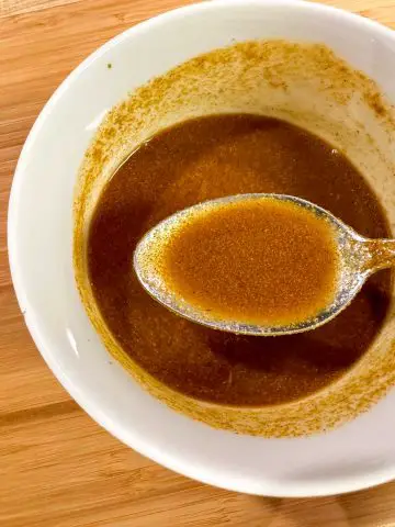 A curry powder based sauce in a white bowl with a spoon containing some of the sauce in the foreground.