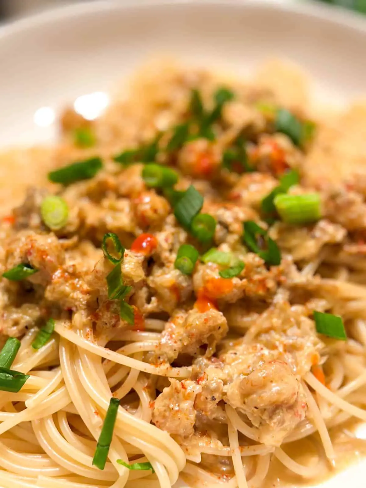 A creamy sauce made with crawfish on top of spaghetti garnished with green onions and drops of Tabasco sauce.