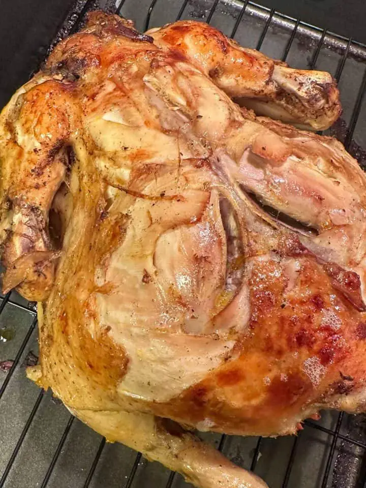A whole chicken on a roasting rack that has been browned in the oven.