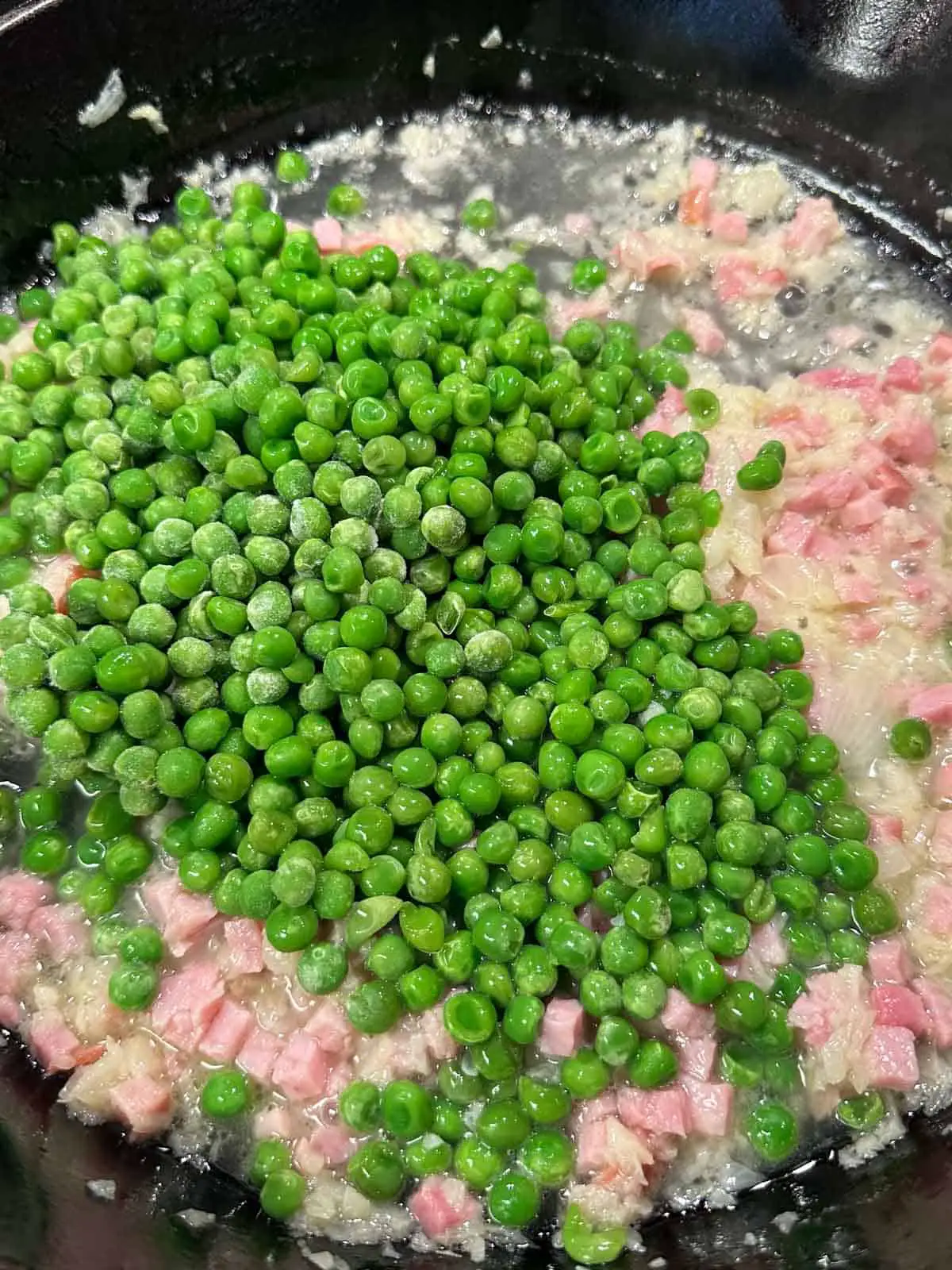 Peas, diced ham, onion, and chicken broth in a cast iron skillet.