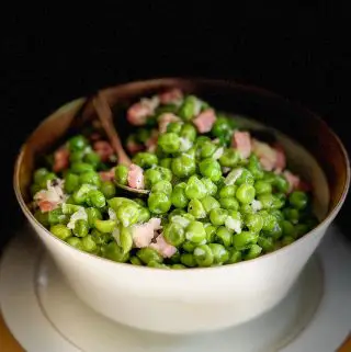 A gold rimmed bowl containing peas, ham, and onion with a gold stemmed spoon resting in the bowl. Part of the picture is in shadow giving it a moody look.